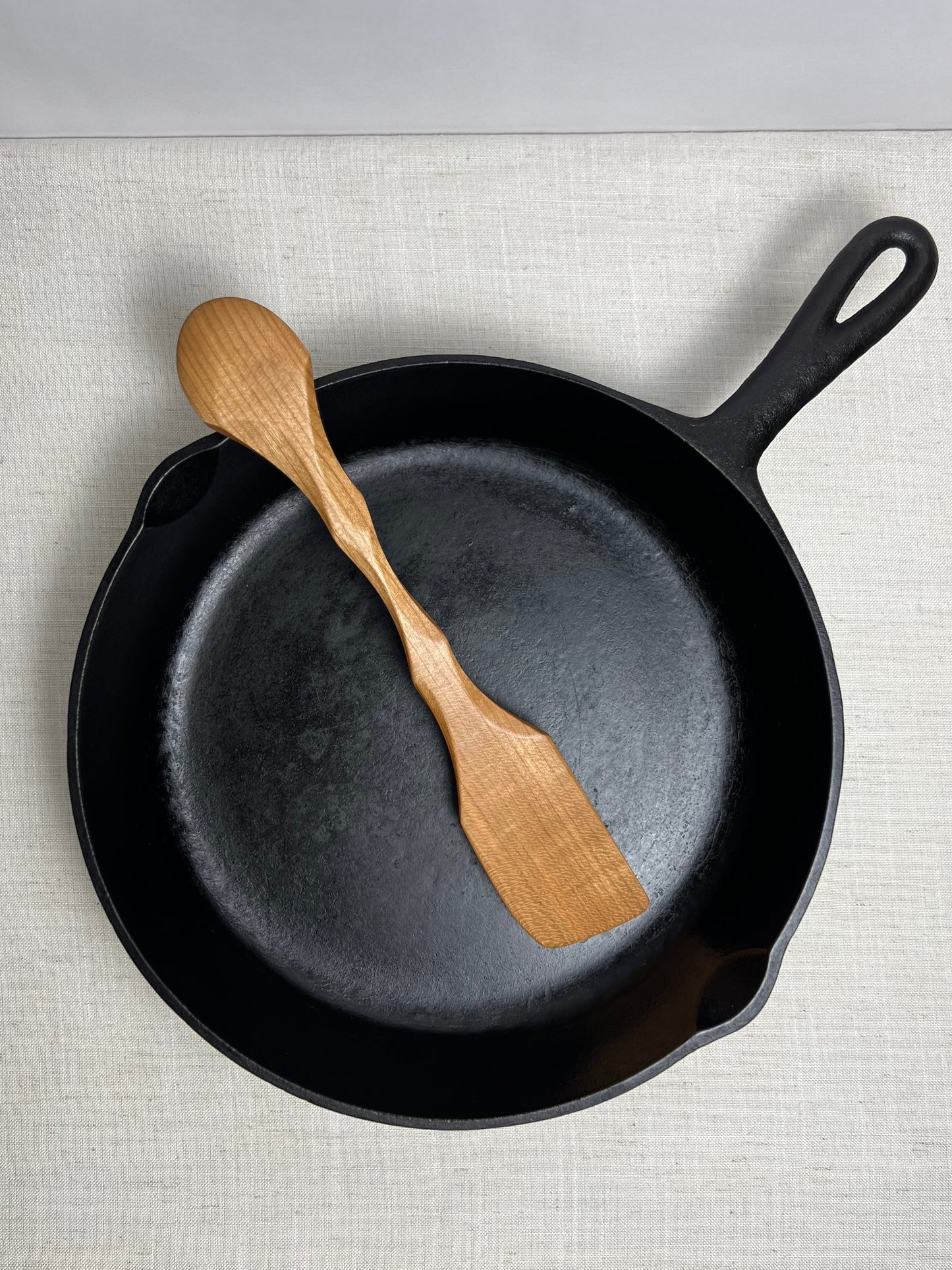 Black cast iron skillet with a wooden spatula on a light gray surface
