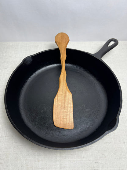 Black cast iron skillet with a wooden spatula on a light gray background