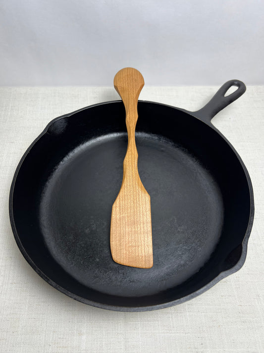Black cast iron skillet with a wooden spatula on a light gray background