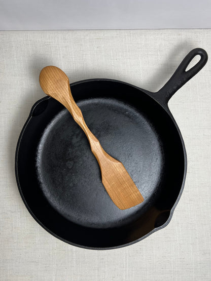 Black cast iron skillet with a wooden spatula on a light gray surface