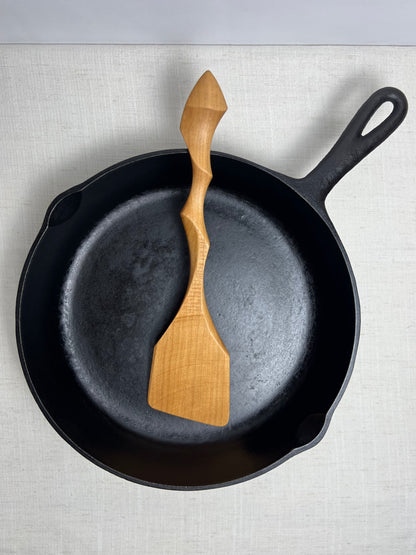 Black cast iron skillet with a wooden spatula on a light gray background