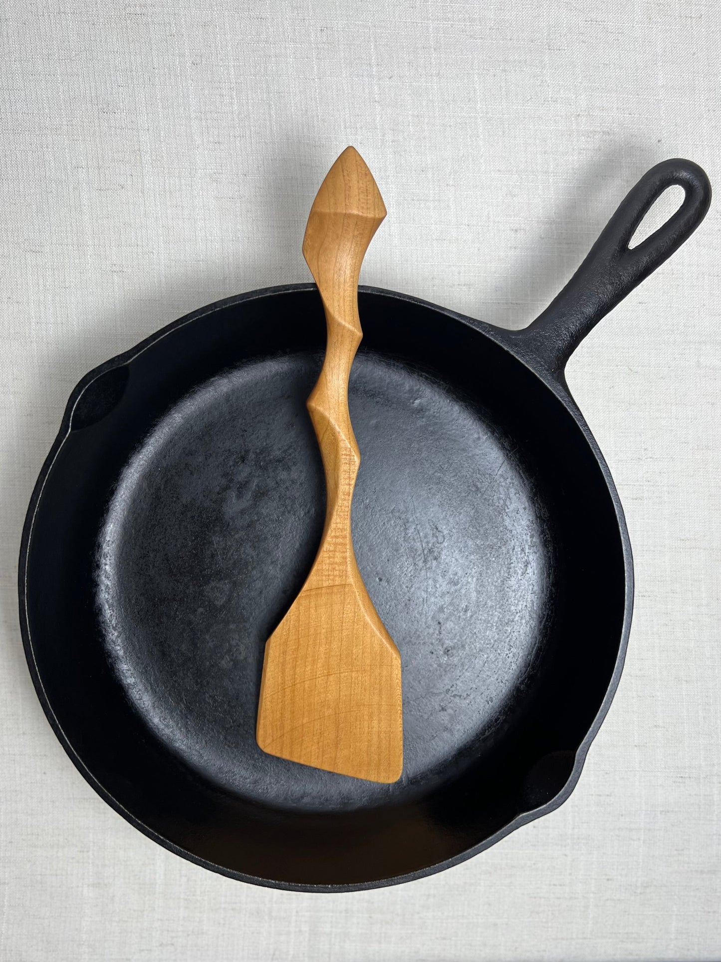 Black cast iron skillet with wooden spatula on a light gray background